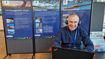 Ole Christian Bjerkemo med hodetelefoner foran plakater om oljevern